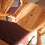 Looking down towards the seat of a rocking chair in order to see details in the shakertape backrest and the complementary colors of the wood and the cotton webbing.