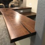 Live-edge black walnut. Mitered at the corner to precisely match grain and color. Matching drop-counter behind the bar. $- Specially Commissioned